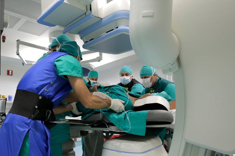 Médicos vestidos de verde manipulan a un paciente bajo un aparato conocido como arco en c, por su forma.