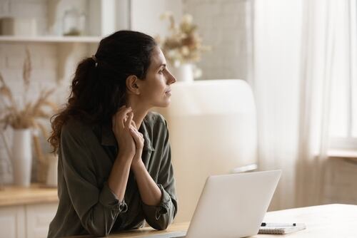 Mujer pensativa frente a una computadora en su hogar, representando la transición hacia el teletrabajo como una tendencia laboral.