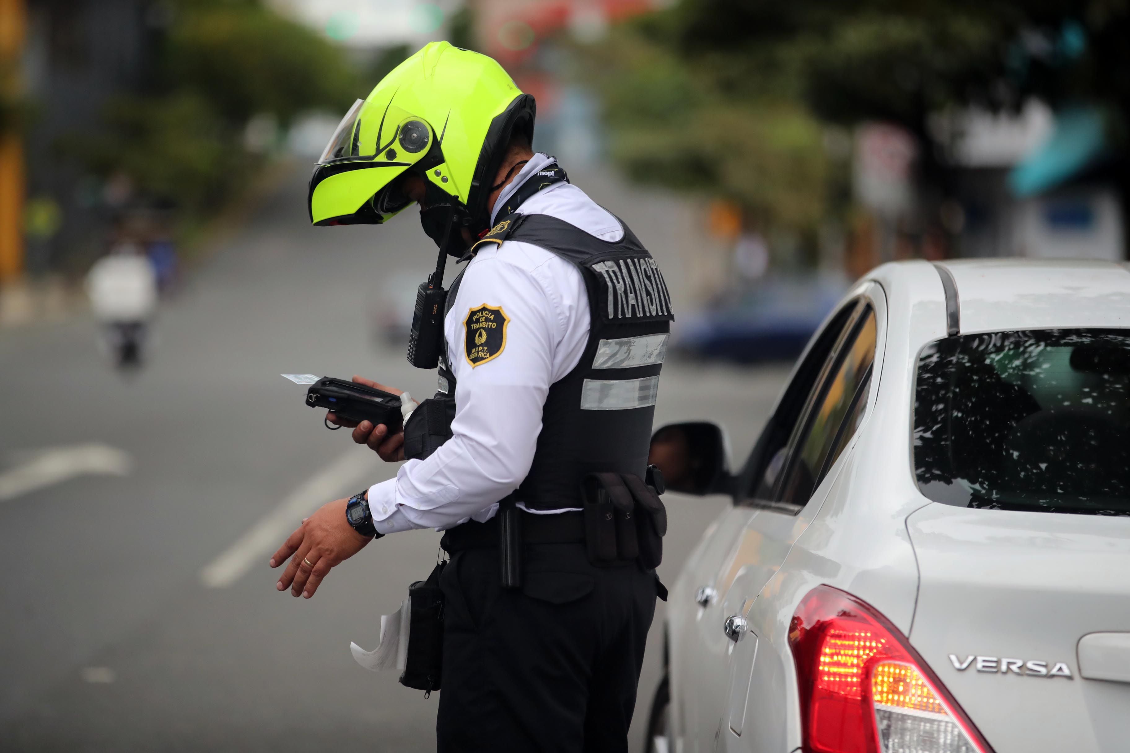 Oficial de la Policía de Tránsito en Costa Rica verifica documentos de un conductor detenido en un operativo de control en carretera.