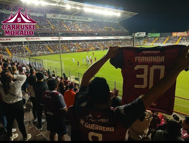 El esposo de María Fernanda Navarro estuvo presente en el estadio con la camiseta de su esposa víctima del accidente en Circunvalación. Foto: Carrusel Morado, Facebook