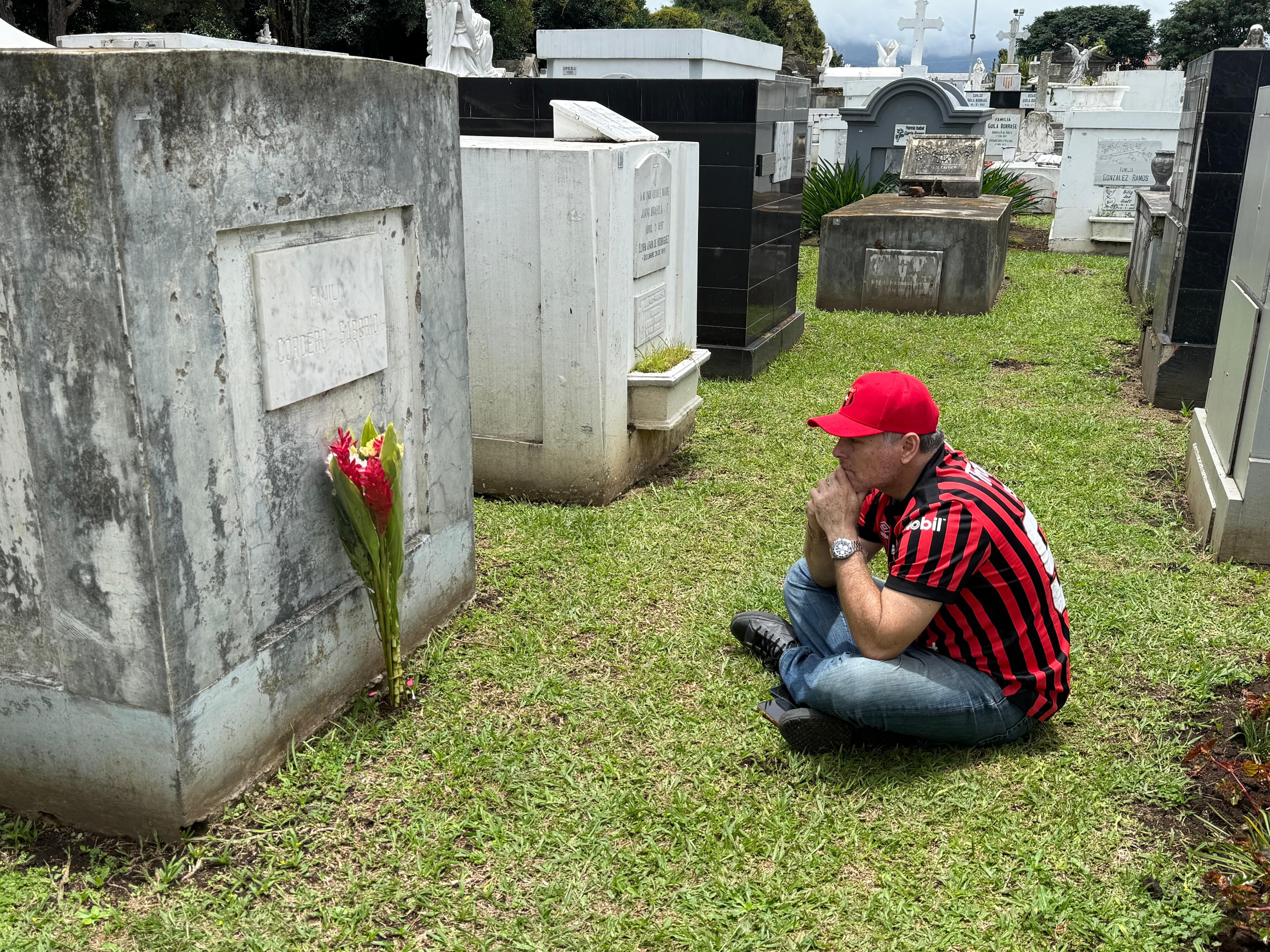 El sábado 15 de agosto del 2026, Día de las Madres, realizamos un recorrido por tres cementerios en San José: el Obreros, el General y el Municipal de Desamparados. En la foto, el aficionado a Alajuelense meditando frente a la tumba de su mamá, doña Elizabeth Cedeño, quien era bien manuda.