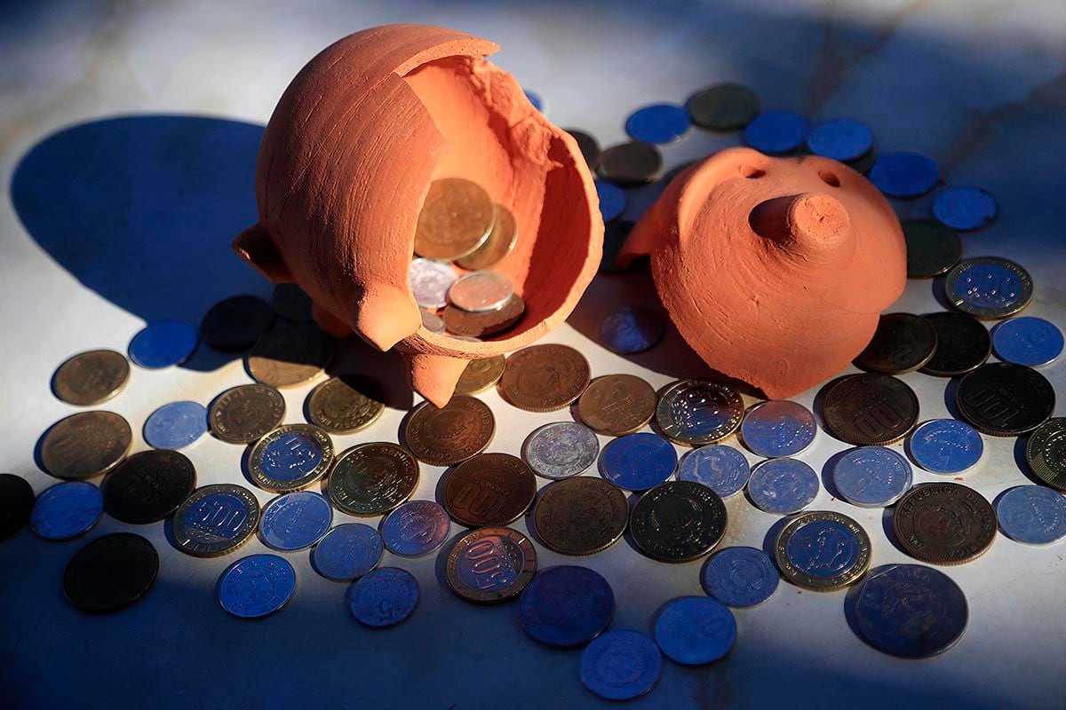 En la imagen se observa una alcancía en forma de chancho, con monedas regadas en el suelo.