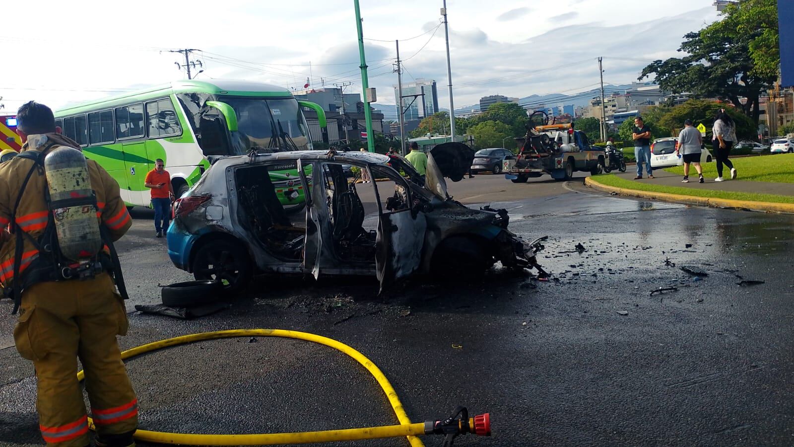 En primer plano, un bombero con su manguera, en segundo plano, el vehículo incendiado. De fondo, el autobús.