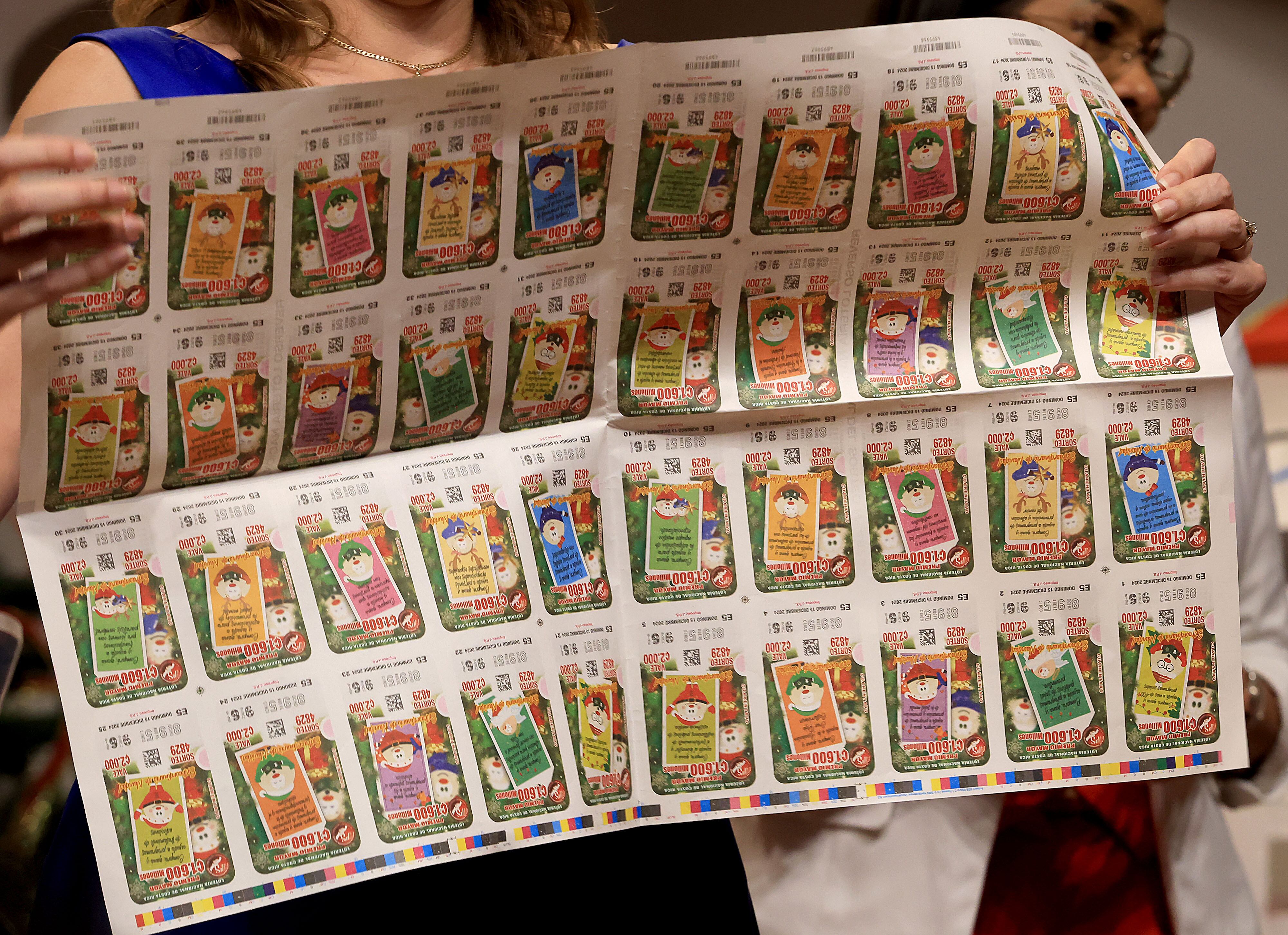Planchas impresas de billetes de la lotería del Gordo Navideño 2024, con diseños coloridos y números en serie, sostenidas por una persona.