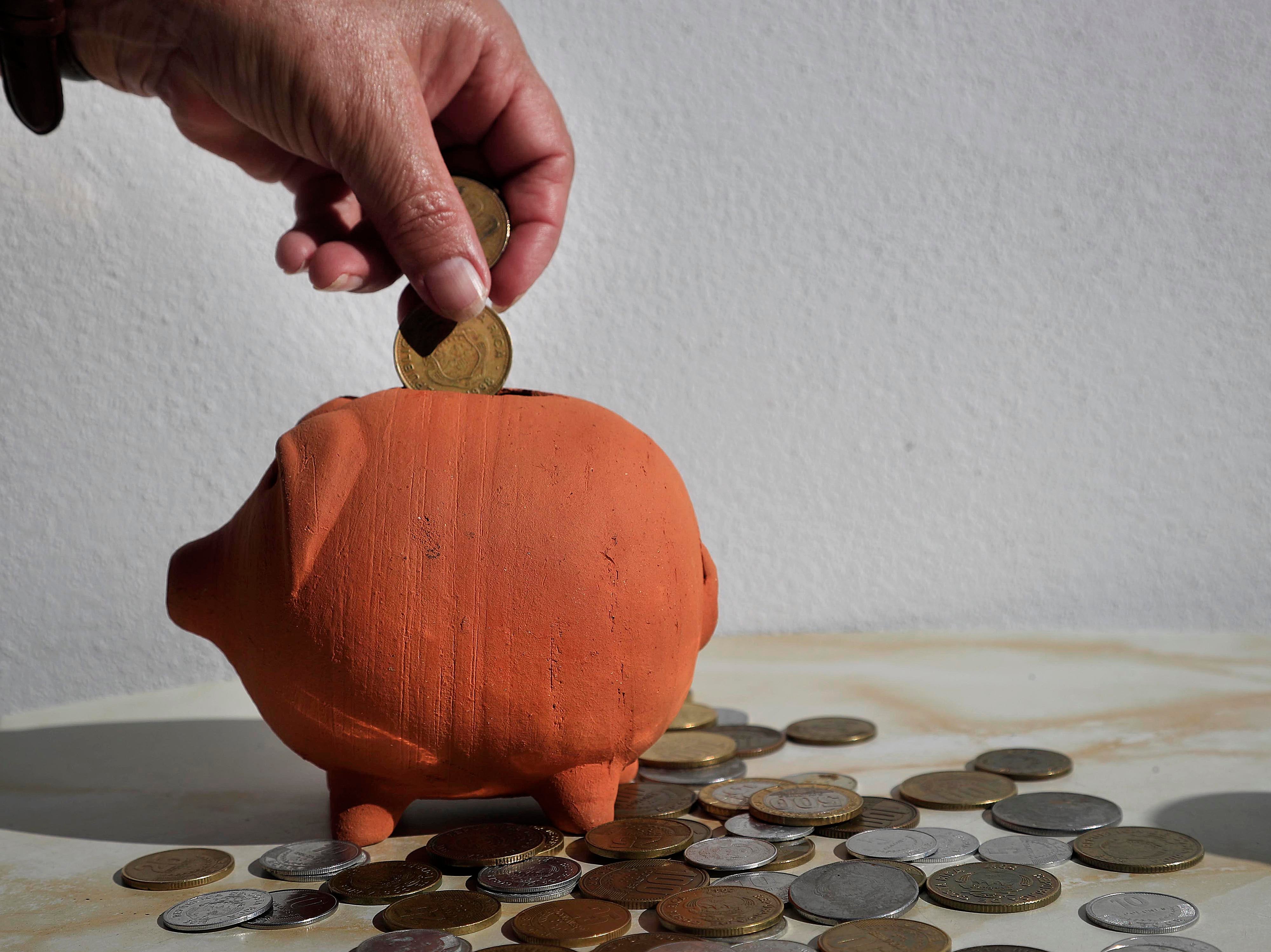 Mano introduciendo monedas en una alcancía de barro, con varias monedas esparcidas alrededor, representando el ahorro y la inversión en certificados de depósito a plazo en Costa Rica.