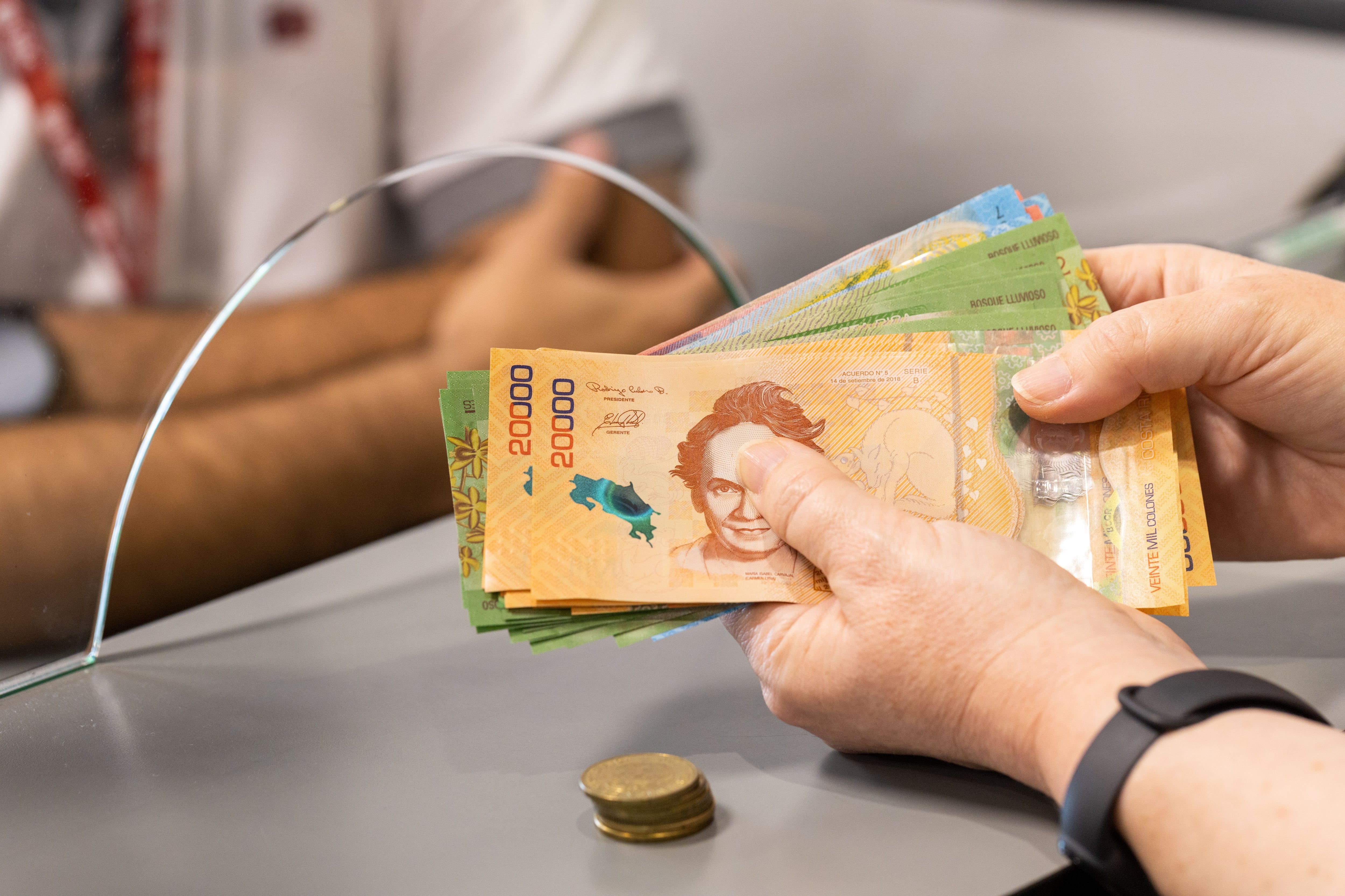 Mano de una persona contando billetes de 20.000 colones en un mostrador, representando la entrega del salario escolar 2025 en Costa Rica.