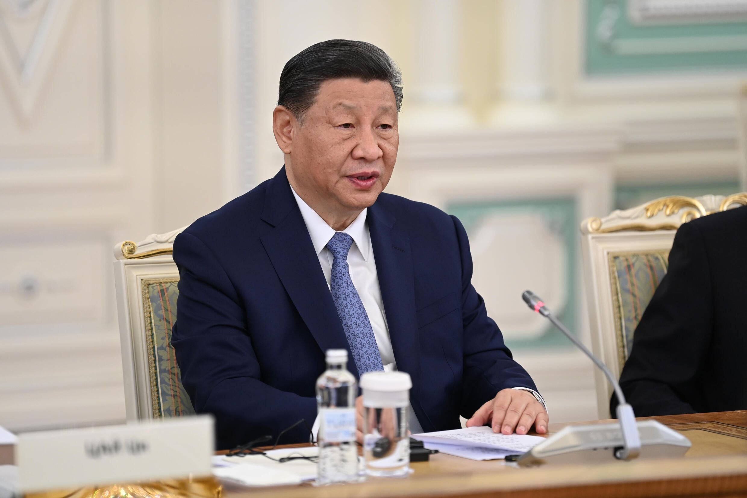 Xi Jinping, presidente de China, sentado en una mesa durante una reunión en Pekín con representantes financieros, vestido con un traje azul y corbata, en un entorno formal.