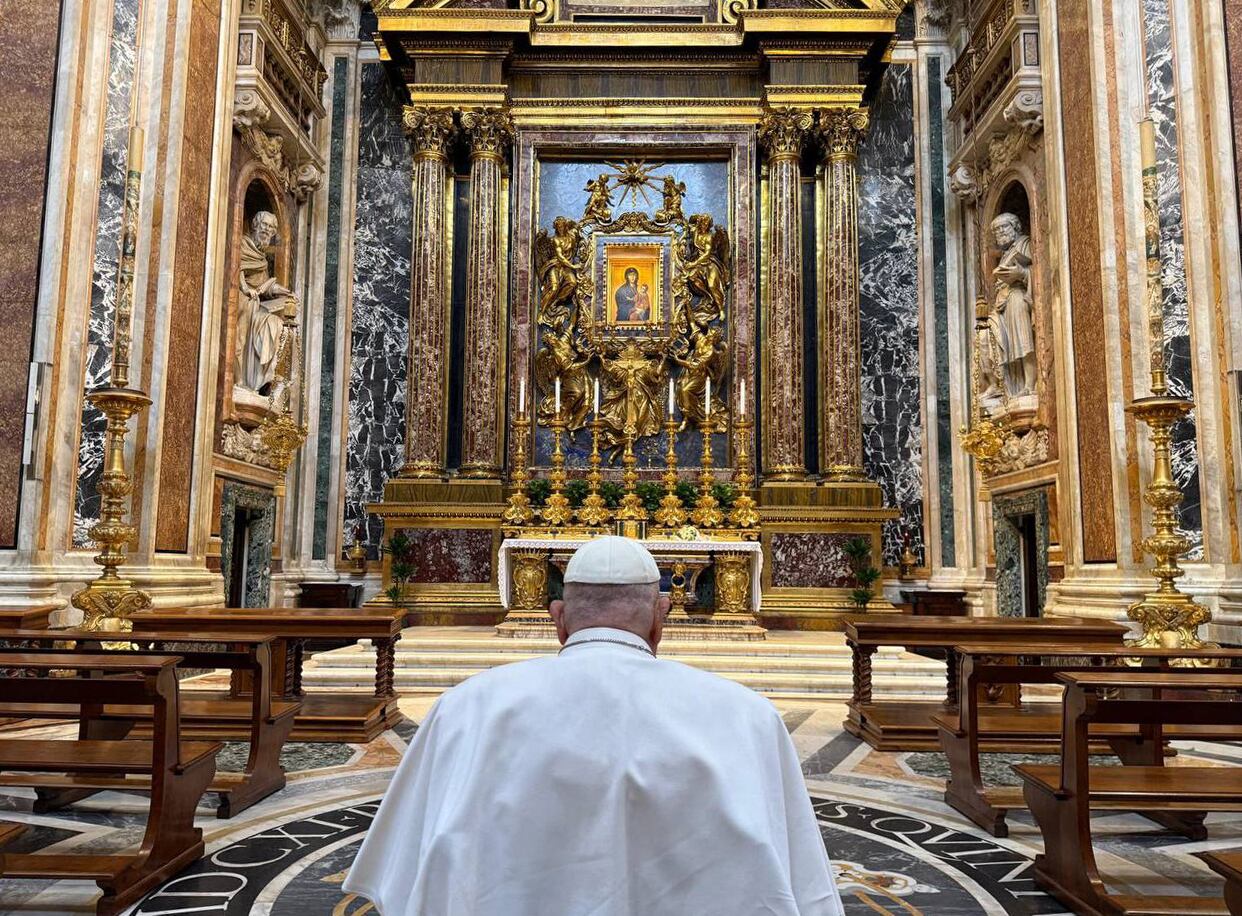 El papa Francisco de espaldas, orando ante un altar.