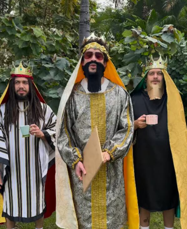 Tres hombres vestidos de manera cómica como los Reyes Magos. En el centro, con una barba falsa, corona, túnica y lentes para el sol, está Bad Bunny sosteniendo su nuevo disco.