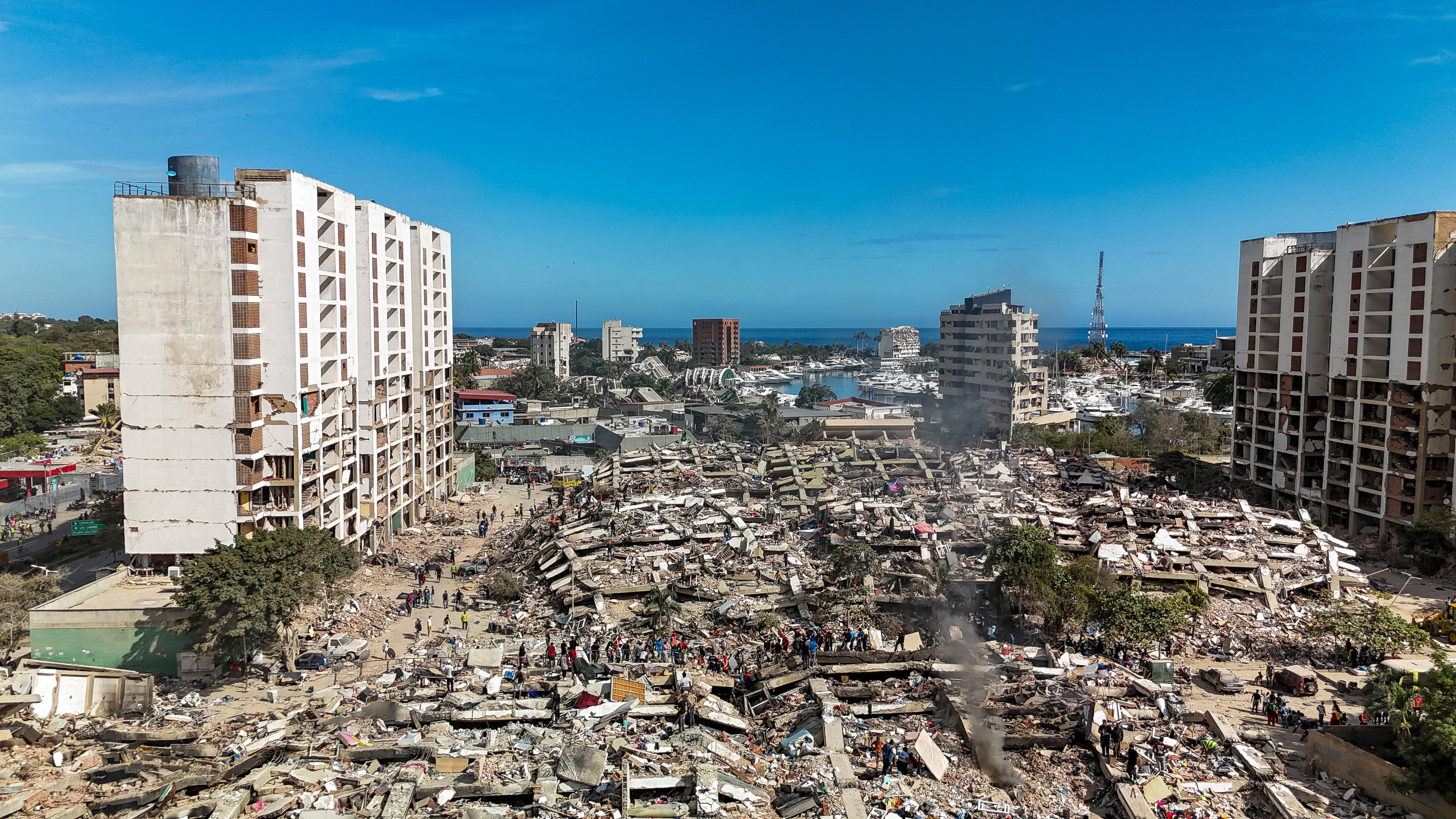 This aerial view shows destroyed buildings in Caraballeda, La Guaira state, Venezuela, on June 28, 2026, following earthquakes. Thousands of rescuers, relatives and volunteers dig day and night through mounds of concrete to find survivors of the earthquakes that struck Venezuela more than three days ago, leaving nearly 1,500 dead and tens of thousands missing. (Photo by Miguel MEDINA / POOL / AFP)