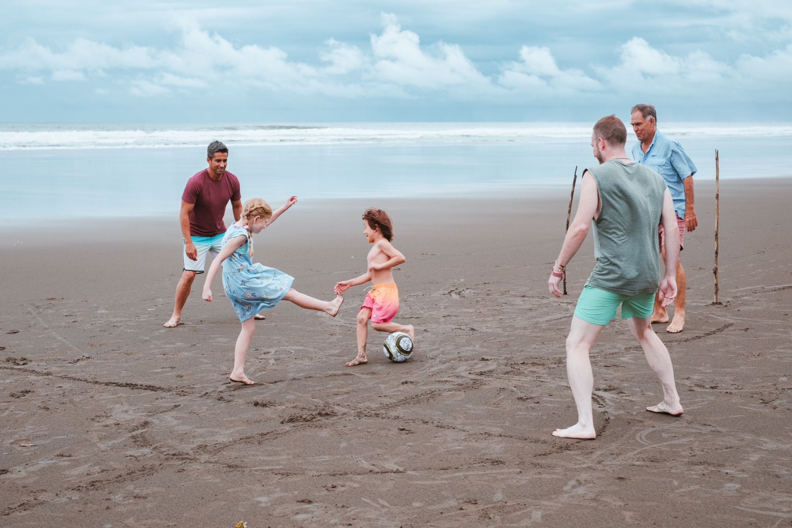 Grupo de personas jugando fútbol en la arena de una playa con el océano de fondo, representando actividades recreativas en Costa Rica.