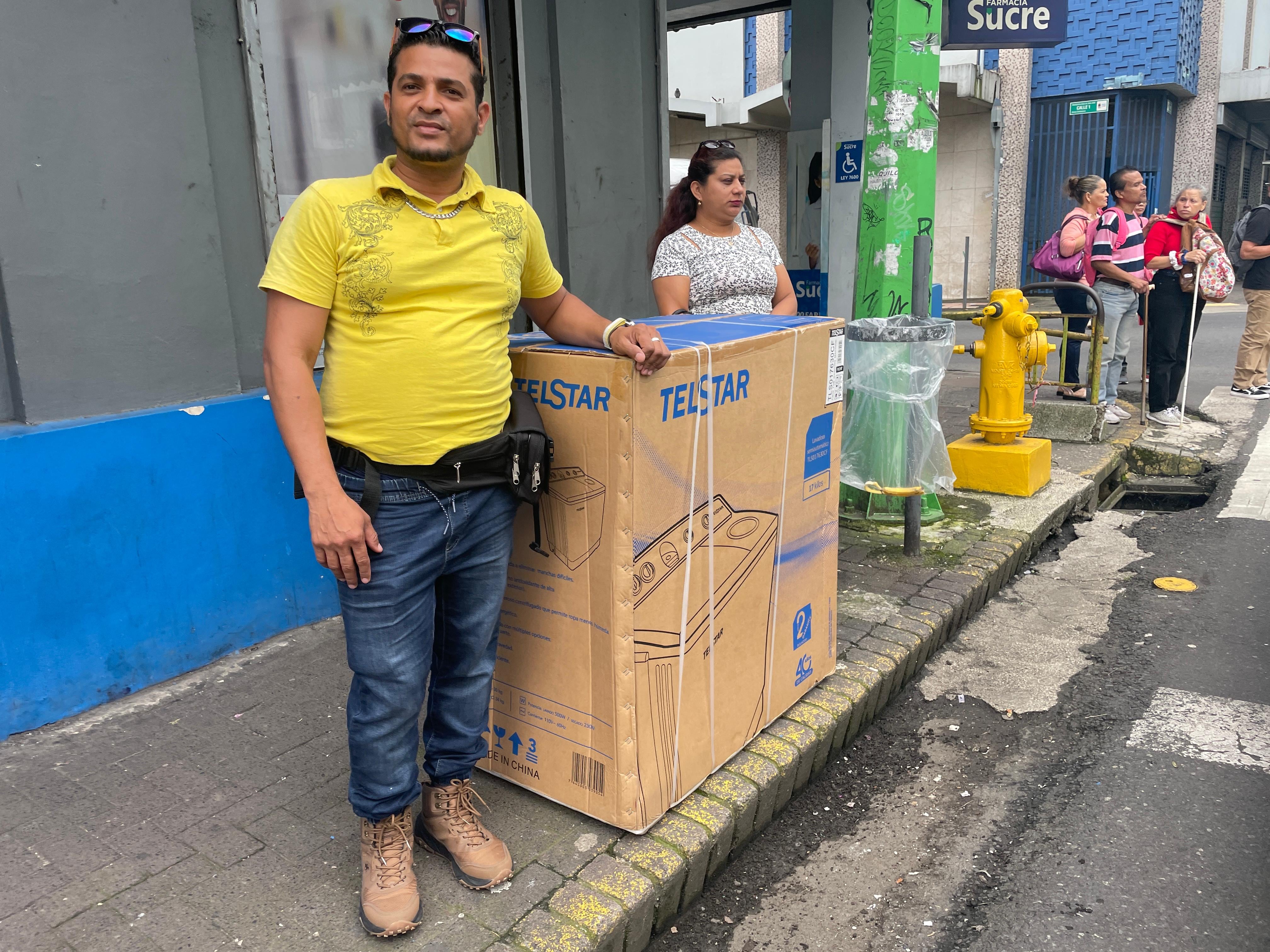 Hombre vestido con camiseta amarilla junto a una caja de lavadora Telstar en una calle de San José, como parte de las promociones del Black Friday.