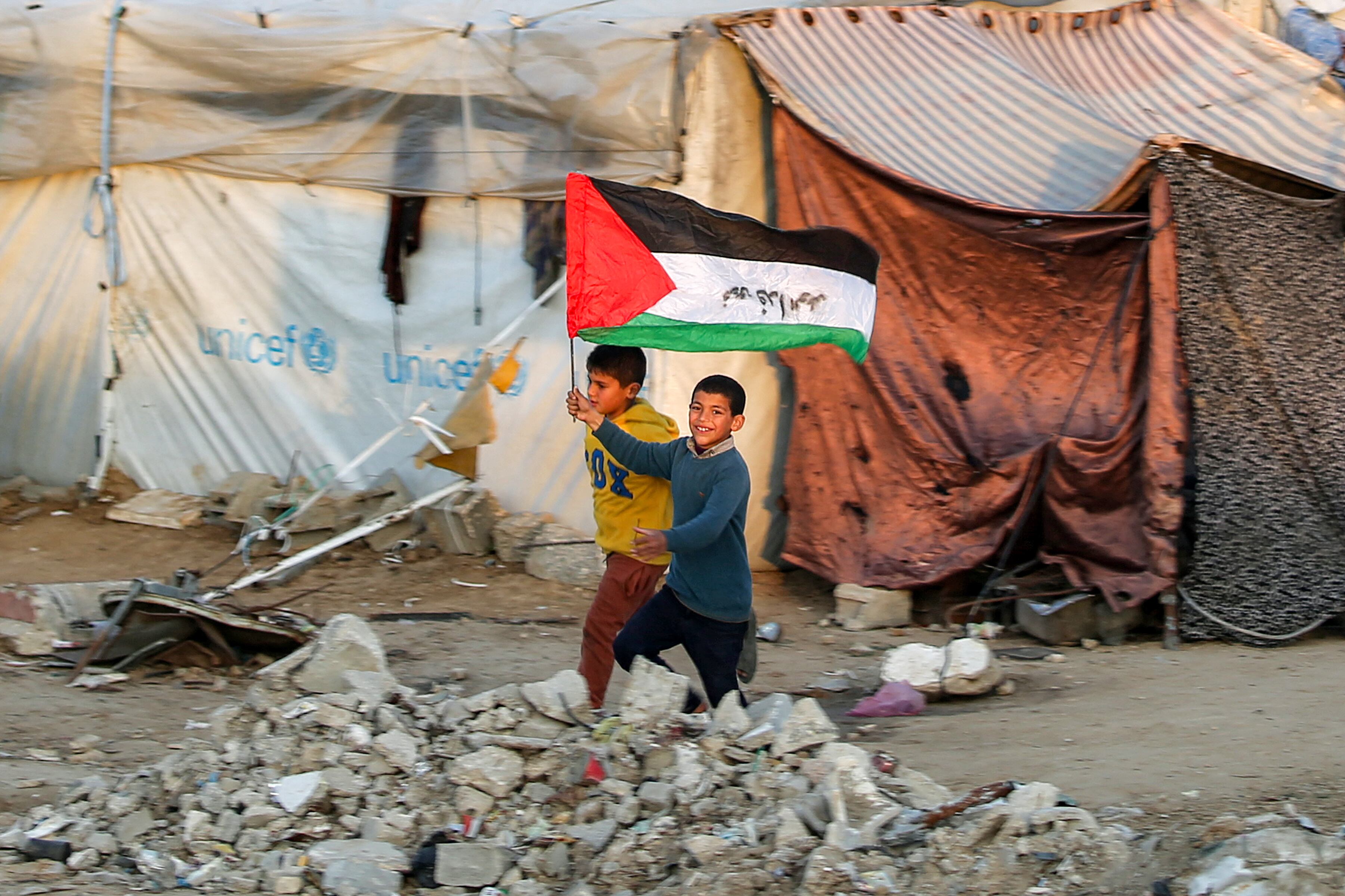 Un niño con una bandera palestina que dice "nos sacrificamos por la nación" corre junto a un campamento de desplazados en Bureij, Gaza, tras el anuncio de una tregua entre Israel y Hamás, el 17 de enero de 2025.