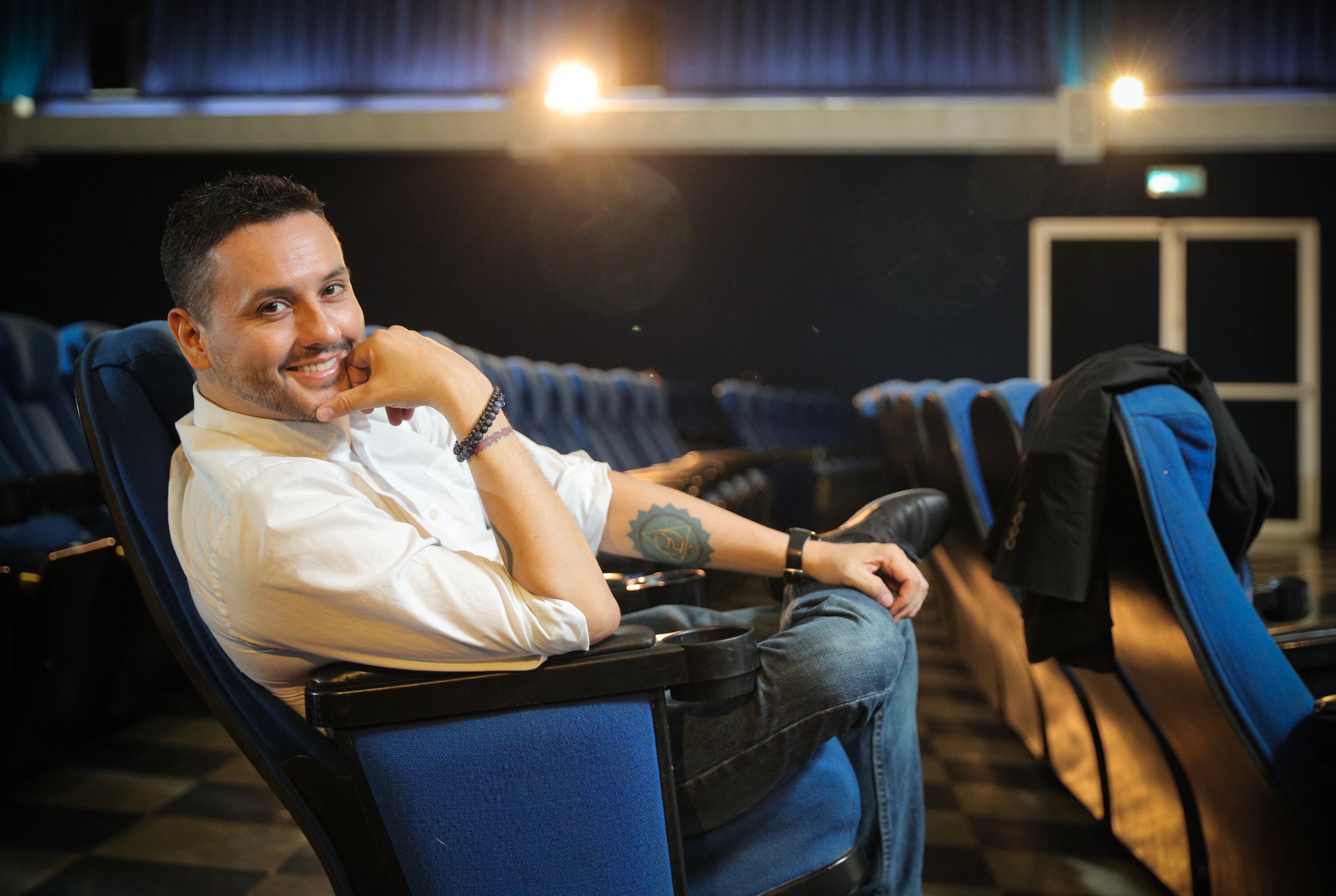 Retrato de Walter Campos sentado en una butaca de cine.  Usa camisa blanca y jeans.