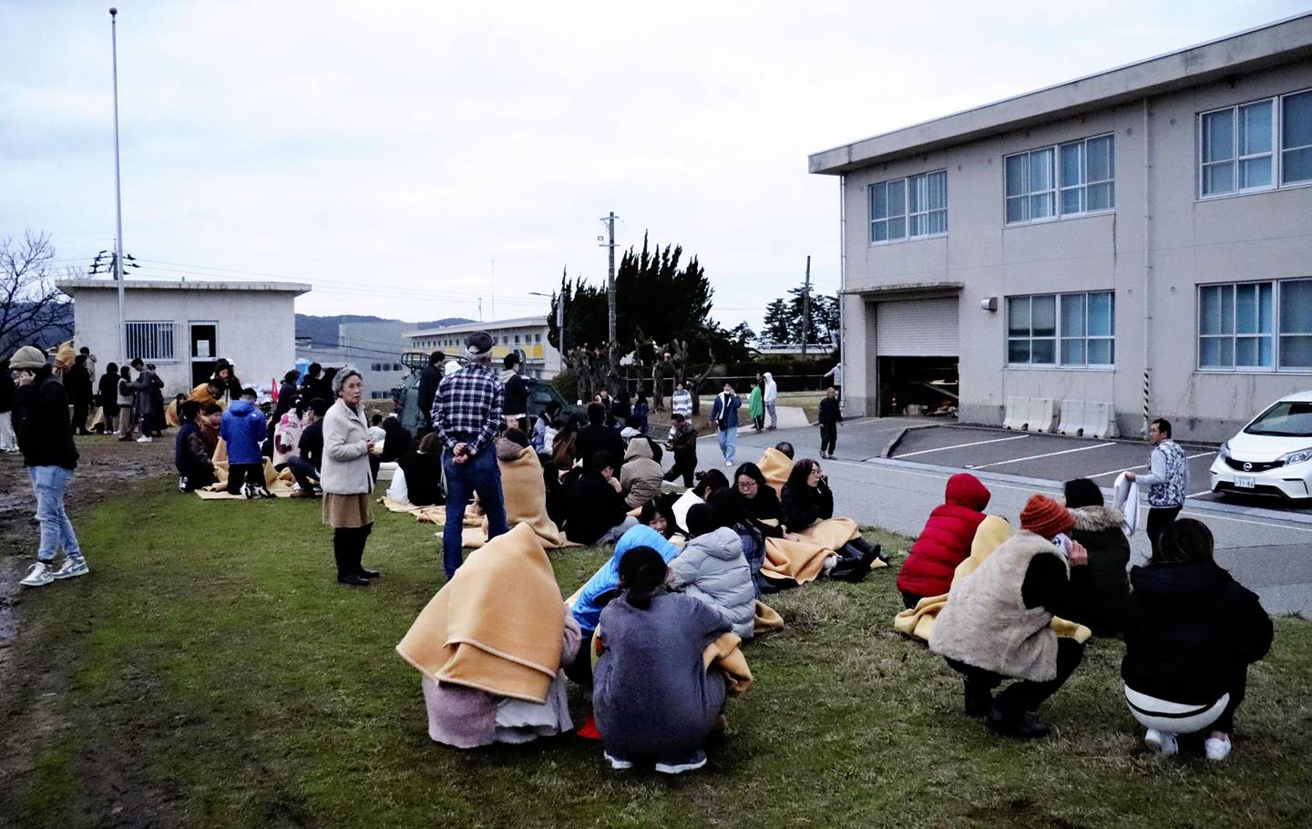 People sit outside in the open after evacuating from buildings in the city of Wajima, Ishikawa prefecture on January 1, 2024, after a major 7.5 magnitude earthquake struck the Noto region in Ishikawa prefecture in the afternoon. Tsunami waves over a metre high hit central Japan on January 1 after a series of powerful earthquakes that damaged homes, closed highways and prompted authorities to urge people to run to higher ground. (Photo by Yusuke FUKUHARA / Yomiuri Shimbun / AFP) / Japan OUT / NO ARCHIVES - MANDATORY CREDIT: Yomiuri Shimbun